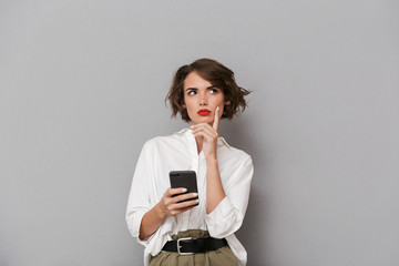 Photo of charming woman 20s smiling and holding mobile phone, isolated over gray background