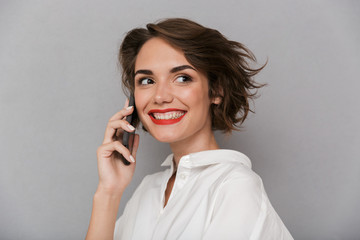 Photo of cute woman 20s smiling and speaking on mobile phone, isolated over gray background