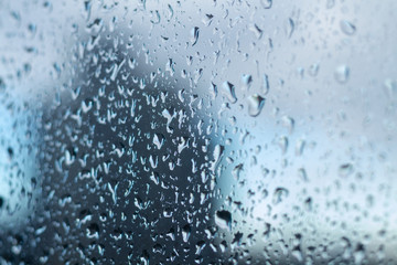 Cold shiny drops of autumn rain on the window pane in rainy autumn weather. Cool background with a sad quiet mood. Crying rain on the glasses.