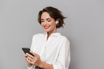Fototapeta premium Photo of adorable woman 20s listening to music on smartphone via earphones, isolated over gray background