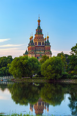Fototapeta premium Orthodox church on the bank of Olgin pond at dusk in low light surrounded by green summer trees of the garden for walking. Peter and Paul Cathedral in Petergof, Saint Petersburg, Russia.