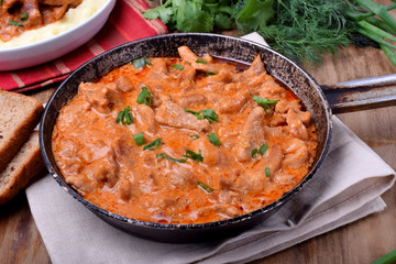 Pieces of meat stewed in tomato and sour cream sauce in the frying pan