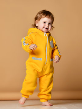 Infant child baby girl kid toddler in winter yellow overalls make first steps happy smiling