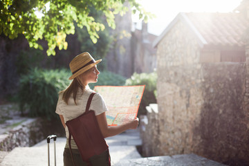 Girl traveler with city map at town street. Woman tourist is searching direction, exploring locations, walking in magic light. Concept of travel, vacation, female tourism, adventure, trip, journey