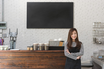 Young woman owner of a cafe stand in front of coffee counter, young entrepreneur conceptual, blank black board on wall