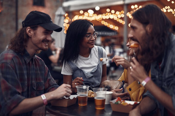 Portrait of young people standing at the table and enjoying meal with drinks. Focus on lovely girl in glasses looking at lady with sleeping pug dog