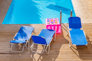 Fototapeta premium Sunbeds by a swimming pool in sunny day. Vacation, summer and relax.