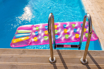 Inflatable colorful mattress in blue swimming pool. Vacation, summer and relax.