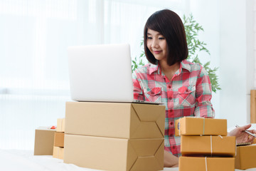 Woman small business owner, business start up in bedroom, young entrepreneur work with laptop prepare parcel boxes for deliver to customer