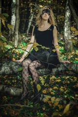 A young kind witch in a black dress with a black mask in a mystical forest in various poses. Art processing