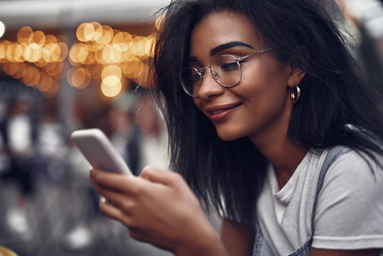 Checking messages. Side view portrait of hipster young lady holding mobile phone and smiling