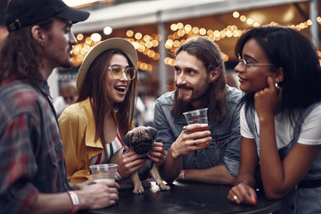 Waist up portrait of stylish hipster friends enjoying drinks while standing at the table. Cheerful...