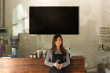 Young woman owner of a cafe stand in front of coffee counter, young entrepreneur conceptual, blank black board on wall