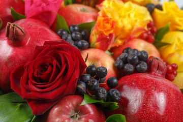 Still life consisting of pomegranates, apples, black rowan, red viburnum, pears, lemons and flowers of red and yellow roses close-up