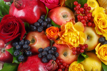 Still life consisting of pomegranates, apples, black rowan, red viburnum, pears, lemons and flowers of red and yellow roses close-up