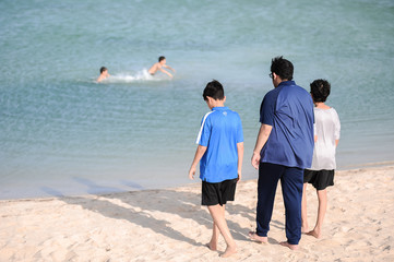 father walks with two sons by the sea and other two boys are swimming in the sea