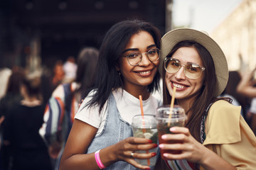 Cheers. Portrait of young ladies in glasses holding drinks and looking at camera with happy smiles