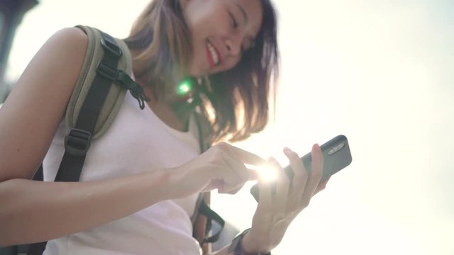 Cheerful Asian backpacker blogger woman using smartphone for direction and looking on location map while traveling at Chinatown in Beijing, China. Lifestyle backpack tourist travel holiday concept.