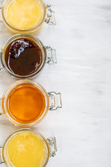 Jars with different kinds of honey in a row on a white wooden background
