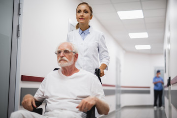 Obraz premium Time for a walk. Portrait of serious bearded gentleman sitting in wheelchair while female medic pushing him. Focus on woman