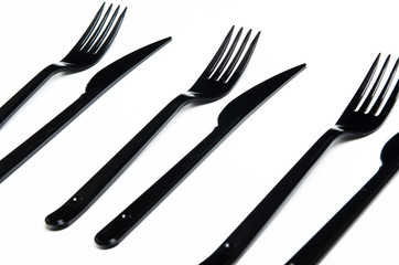 Clean plastic black forks and knives on white background. Disposable dishes, environmental...
