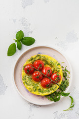 Frittata with arugula, potatoes and cherry tomatoes in iron pan on old stone table background. Top view.