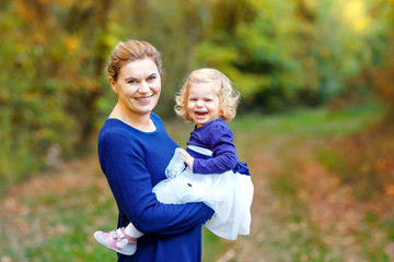 Happy young mother having fun cute toddler daughter, family portrait together. Woman with beautiful baby girl in nature and forest. Mum with little child outdoors, hugging. Love, bonding.