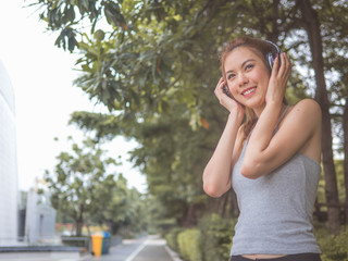 Young beautiful asia woman outdoor in city back light listening music with head phone and smart phone hand hold