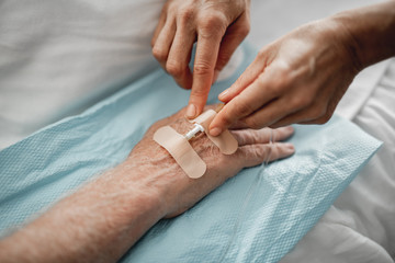 Close up of female hands putting sticking plaster on man arm to fixate needle for IV infusion....