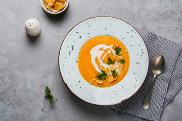 Pumpkin soup with cream, pieces of bread and cedar nuts in gray ceramic plate on gray table background. Traditional autumn food. Top view copy space.