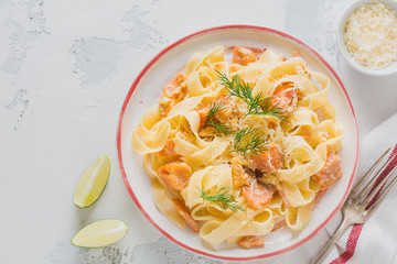 Fettucine pasta with salmon and parmesan cheese in creamy sauce in ceramic plate on old light concrete background. Top view.