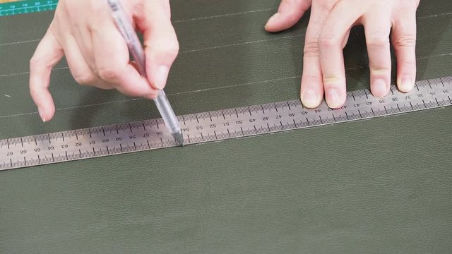 craftsman draws a sketch on green leather using ruller and pen