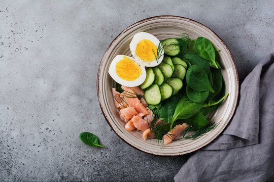 Scandinavian salad with smoked pink salmon, spinach, cucumber and chicken egg in gray ceramic dish. Top view.