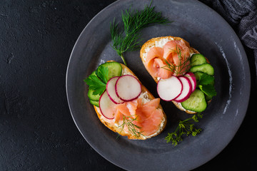 Sandwiches with smoked pink salmon, radish, cucumber and cream cheese on gray ceramic plate and textile background. Traditional Scandinavian toast. Top view.