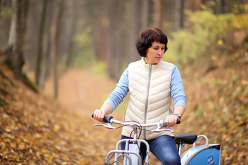 Fototapeta na wymiar The girl on a bike from the rental in the forest. Beautiful young woman posing for the camera in the autumn forest. 