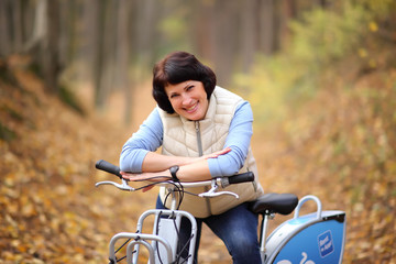 Obraz premium The girl on a bike from the rental in the forest. Beautiful young woman posing for the camera in the autumn forest. 