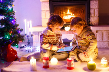 Two cute toddler boys, blond twins playing with new tablet gift. Family celebrating Christmas holiday