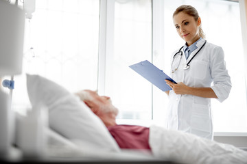 I am checking your condition. Portrait of young lady in white lab coat holding clipboard and...