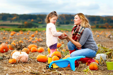 Little kid girl and mother having fun on pumkin field