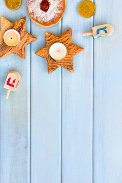 Wooden candlesticks in the shape of star, donut, golden chocolate coins and dreidels on background of blue painted wooden planks with space for text. Jewish holiday Hanukkah. Top view, flat lay