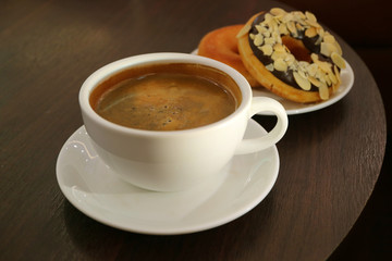 A cup of hot coffee with blurred doughnuts served on dark color wooden table 