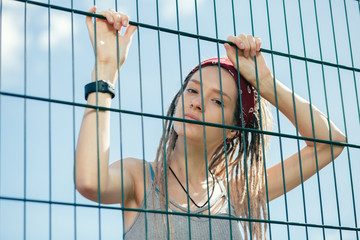 Peaceful tired lady leaning on the chain link fence and looking at you