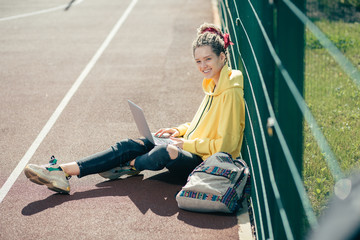 Happy student sitting on the ground and smiling while holding her laptop