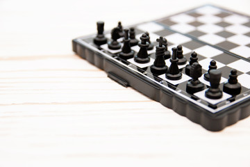 small pocket chess, plastic chess pieces placed on a chessboard on a white wooden background