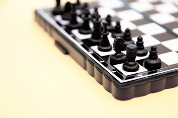 small pocket chess, plastic chess pieces placed on a chessboard on a yellow background