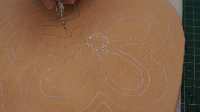 craftsman prepares the pattern on  leather for carving by awl
