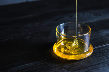 honey flows down in the glass transparent bowl installed on a black wooden background. concept for sugar epilation