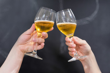 Two friends toasting with glasses of beer at the pub. Blackboard background.