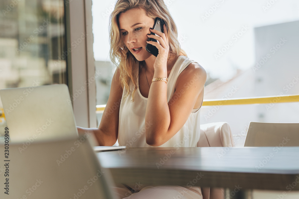 Wall mural Businesswoman talking with client over phone in cafe