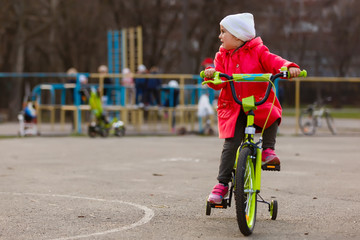 Little girl in red riding a bicycle at a sporting ground